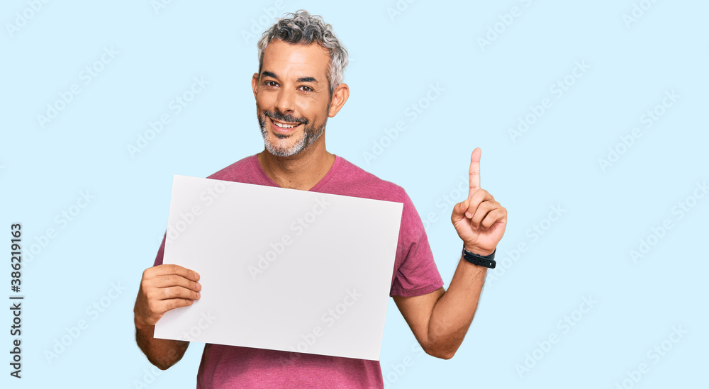 Middle age grey-haired man holding blank empty banner surprised with an idea or question pointing finger with happy face, number one Middle age grey-haired man holding blank empty banner surprised with an idea or question pointing finger with happy face, number one