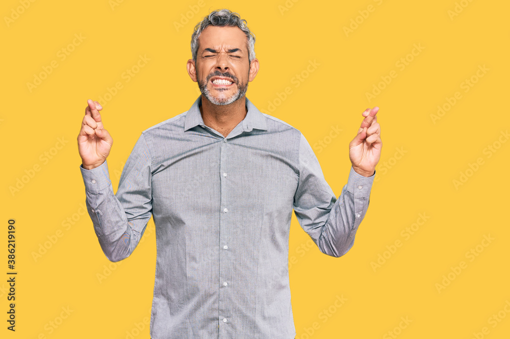 Middle age grey-haired man wearing casual clothes gesturing finger crossed smiling with hope and eyes closed. luck and superstitious concept.
