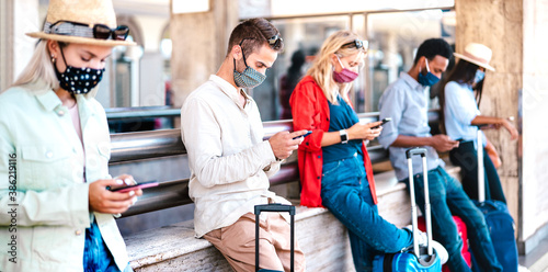 Multiracial friends wearing face mask using mobile smart phones - Young millenial checking online reservations at train station - New normal travel and lifestyle concept - Vivid contrast filter