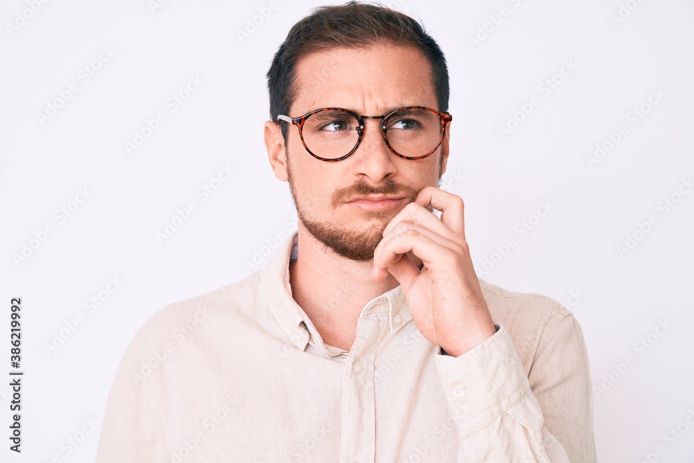 Young handsome man wearing casual clothes and glasses serious face thinking about question with hand on chin, thoughtful about confusing idea
