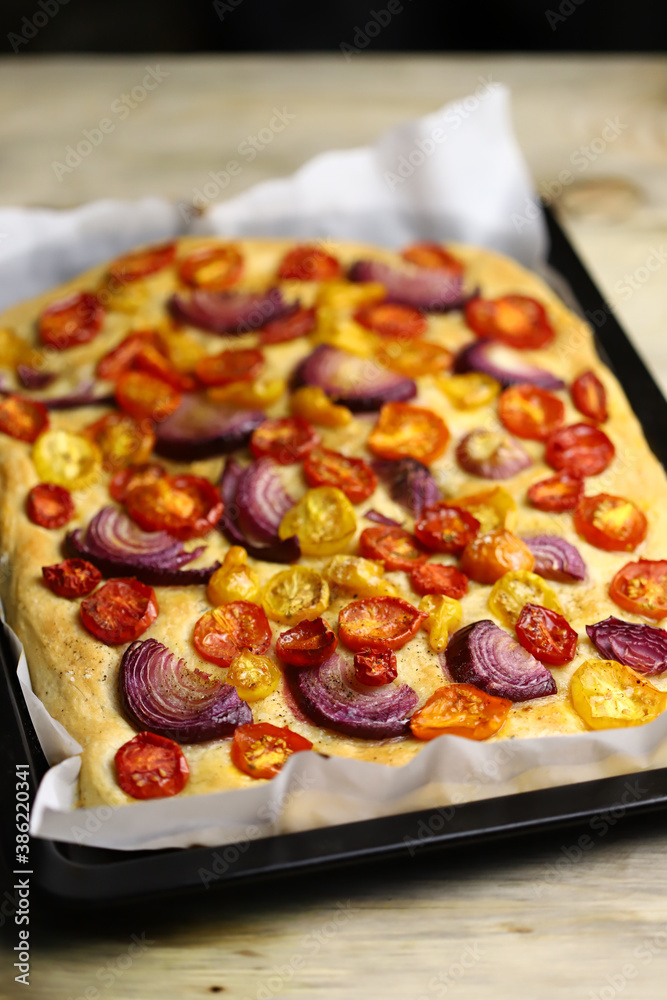 Fresh homemade focaccia on a pan with tomatoes and blue onions. Italian cuisine at home. Focaccia recipe.