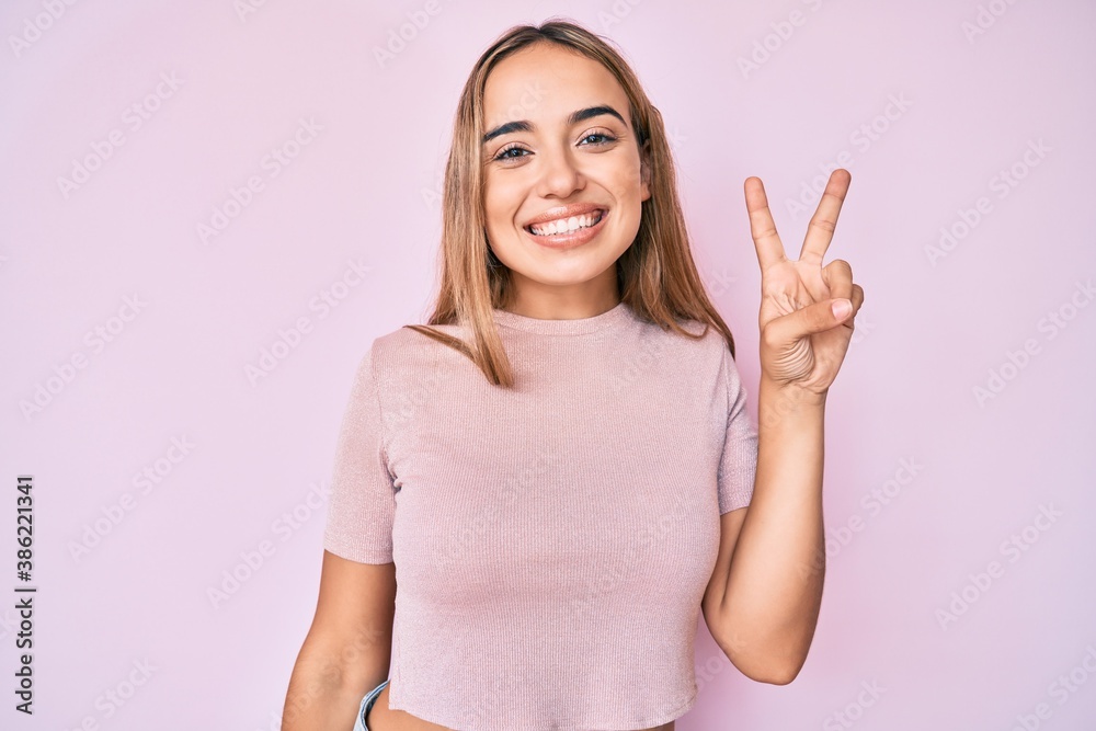 Young beautiful blonde woman wearing casual clothes smiling with happy face winking at the camera doing victory sign. number two. Young beautiful blonde woman wearing casual clothes smiling with happy face winking at the camera doing victory sign. number two.
