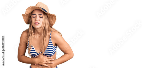 Young beautiful blonde woman wearing bikini and hat with hand on stomach because indigestion, painful illness feeling unwell. ache concept. photo