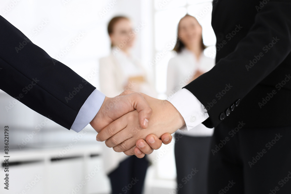 Businessman and woman shaking hands with colleagues at the background. Handshake at meeting in office. Concept of success in business