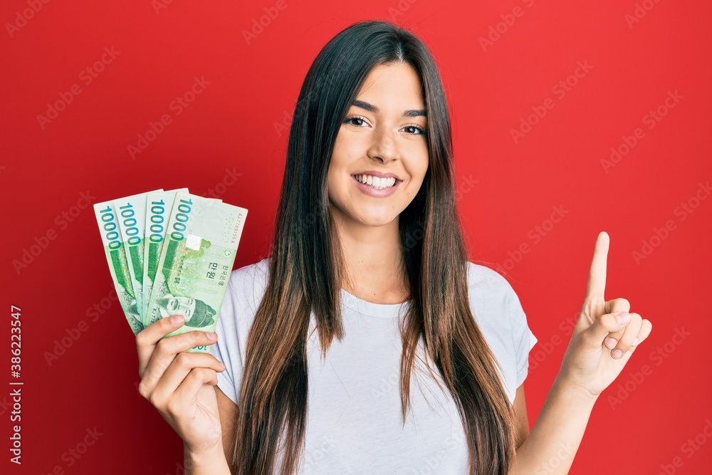 Young brunette woman holding 1000 south korean won banknotes smiling with an idea or question pointing finger with happy face, number one Young brunette woman holding 1000 south korean won banknotes smiling with an idea or question pointing finger with happy face, number one