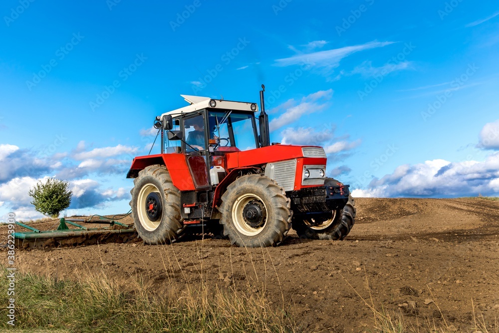 Agriculture red tractor cultivating field over blue sky. Old red tractor in the agricultural field; mechanism. Tractor plowing land. Harvester sowing wheat. Agriculture red tractor cultivating field over blue sky. Old red tractor in the agricultural field; mechanism. Tractor plowing land. Harvester sowing wheat.