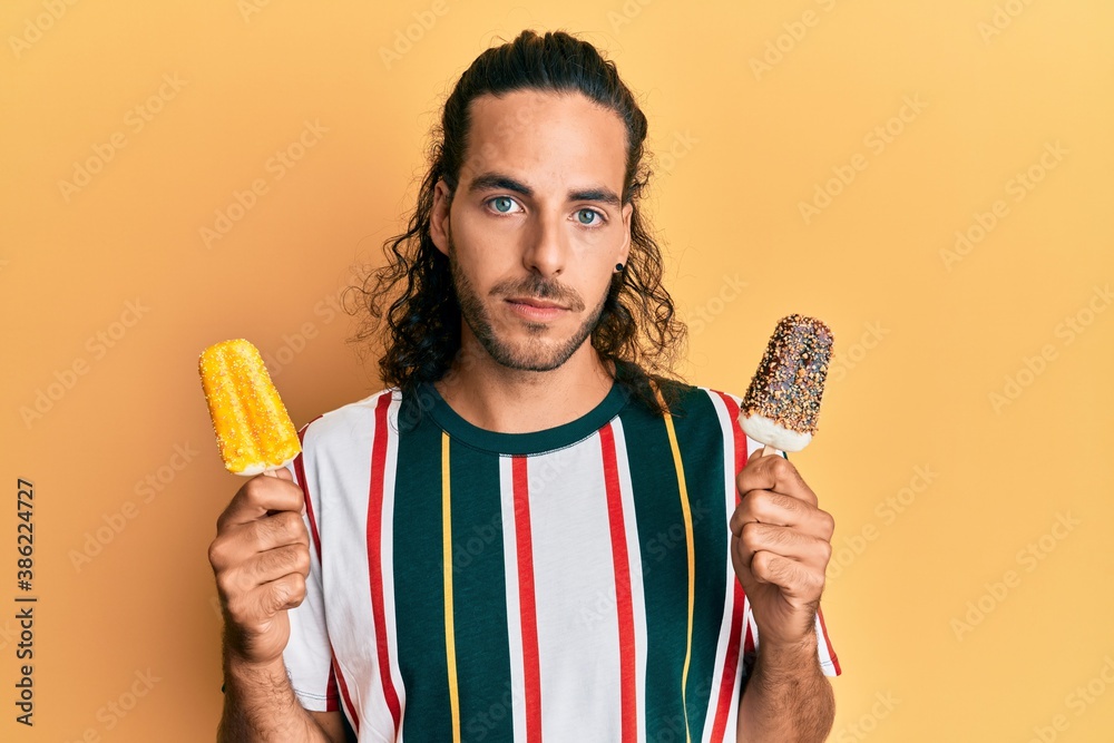 Young handsome man with long hair eating two ice cream relaxed with serious expression on face. simple and natural looking at the camera. Young handsome man with long hair eating two ice cream relaxed with serious expression on face. simple and natural looking at the camera.
