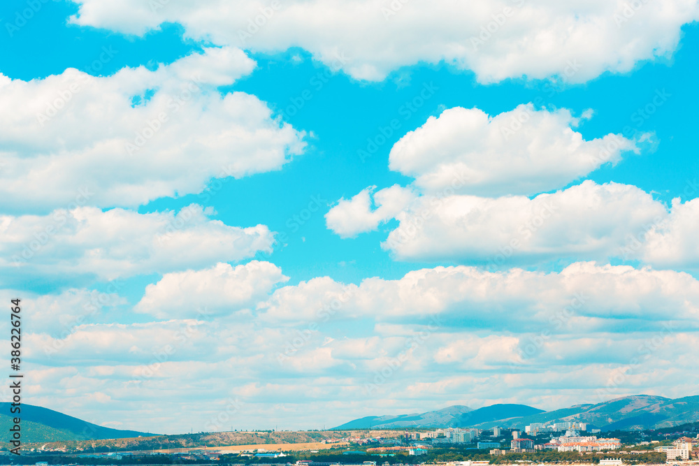 Landscape. Blue bright sky with white cumulus clouds over a mountain valley with a settlement Landscape. Blue bright sky with white cumulus clouds over a mountain valley with a settlement