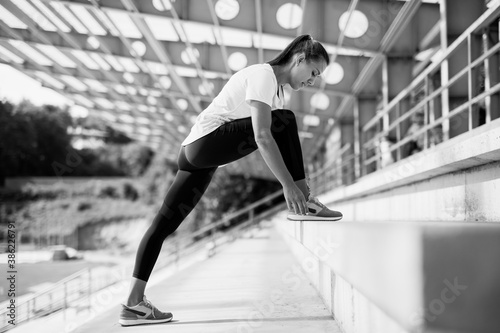 Young fitness woman in sportswear stretching legs on stairs