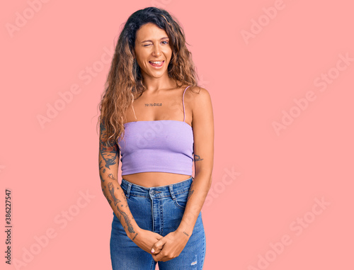 Young hispanic woman with tattoo wearing casual clothes winking looking at the camera with sexy expression, cheerful and happy face.