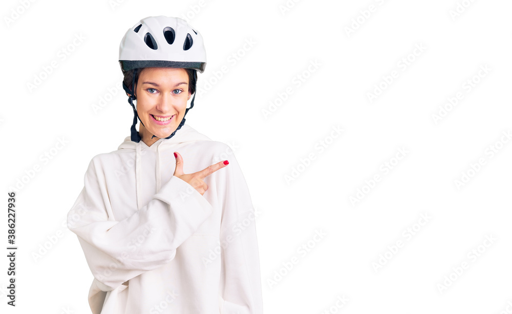 Beautiful brunette young woman wearing bike helmet and sporty clothes cheerful with a smile of face pointing with hand and finger up to the side with happy and natural expression on face Beautiful brunette young woman wearing bike helmet and sporty clothes cheerful with a smile of face pointing with hand and finger up to the side with happy and natural expression on face