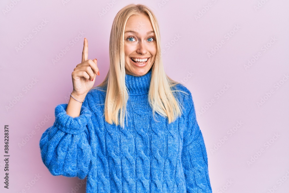 Young blonde girl wearing wool winter sweater pointing finger up with successful idea. exited and happy. number one. Young blonde girl wearing wool winter sweater pointing finger up with successful idea. exited and happy. number one.