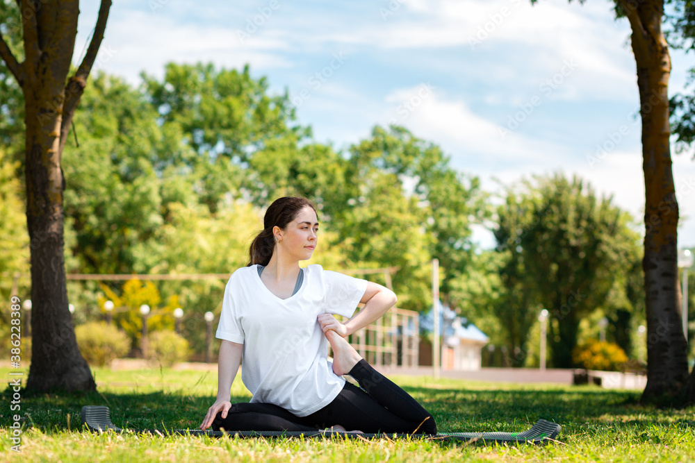 Yoga. A young woman in sports clothes, doing an exercise in the Park on the grass. Side view. The concept of sport for a healthy lifestyle Yoga. A young woman in sports clothes, doing an exercise in the Park on the grass. Side view. The concept of sport for a healthy lifestyle