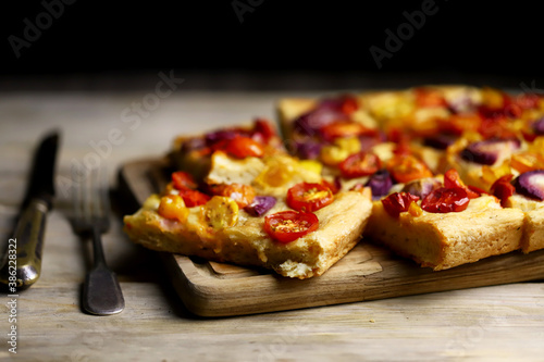 Selective focus. Macro. Fresh homemade focaccia with tomatoes and blue onions. Italian cuisine at home. Focaccia recipe. Rustic style.