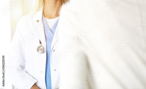 Unknown woman-doctor communicating with female patient in sunny clinic. Physician checks medical history record and exam results, close-up