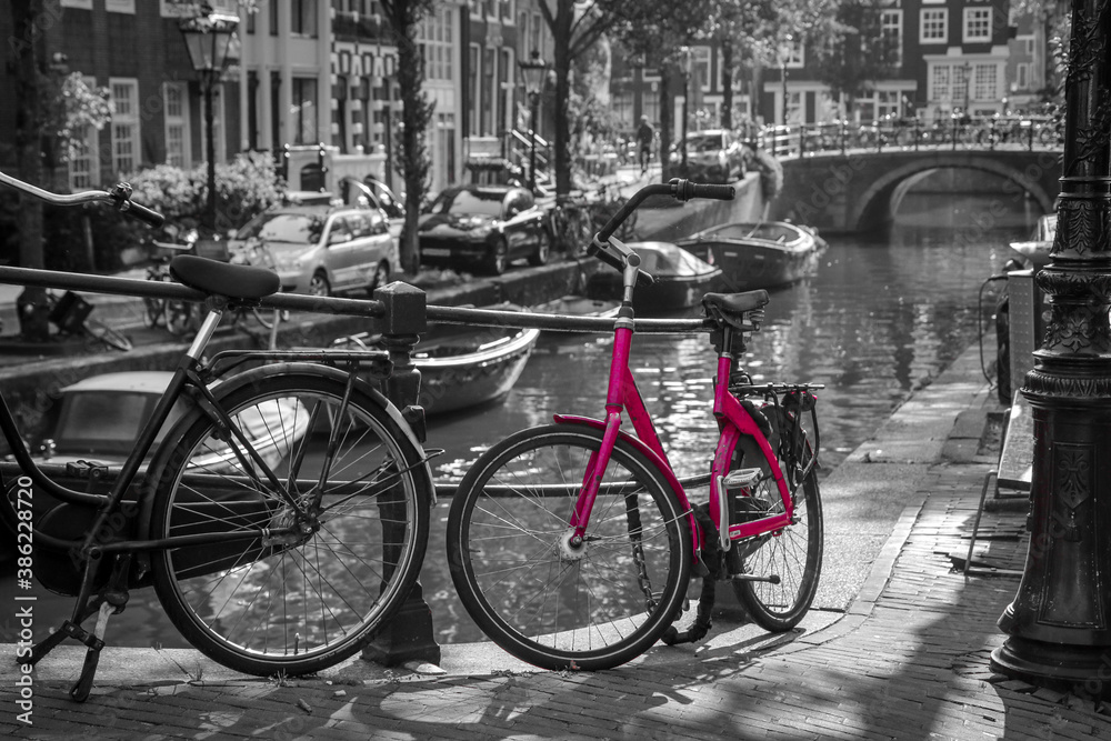 A picture of a pink bike on the bridge over the channel in Amsterdam. The background is black and white.