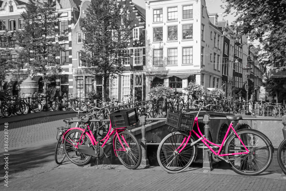 A picture of two pink bikes on the bridge over the channel in Amsterdam. The background is black and white.