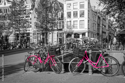 A picture of two pink bikes on the bridge over the channel in Amsterdam. The background is black and white.