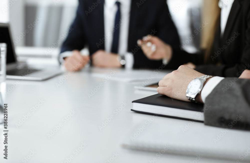 Unknown businessmen and woman sitting, working and discussing questions at meeting in modern office, close-up