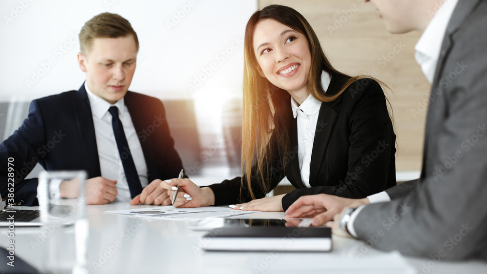 Businessman and woman with colleague sitting and working at meeting in sunny office Businessman and woman with colleague sitting and working at meeting in sunny office