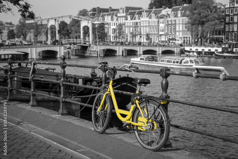 A picture of a lonely yellow bike on the bridge over the channel in Amsterdam. The background is black and white.
