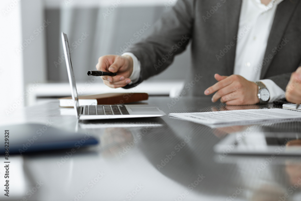 Unknown businessmen and woman sitting, working and discussing questions at meeting in modern office, close-up Unknown businessmen and woman sitting, working and discussing questions at meeting in modern office, close-up