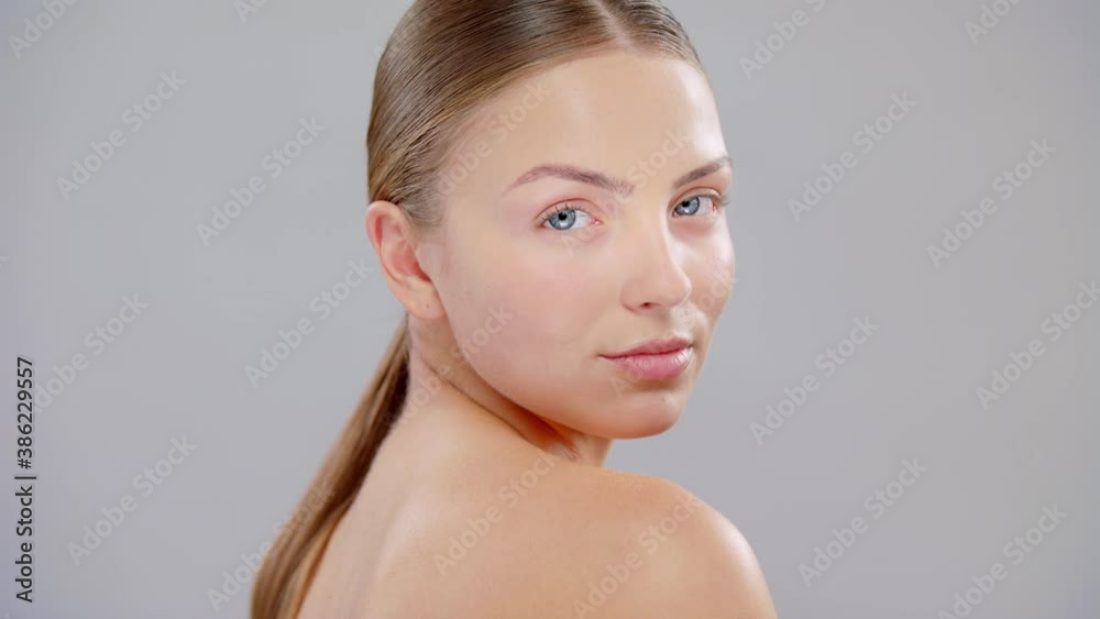Close Up Beautiful Young Caucasian Blonde Woman With Blue Eyes And Smooth Healthy Skin Looking To The Camera Skin Care Cosmetic Concept. Slow Motion On Grey Background. Close Up Beautiful Young Caucasian Blonde Woman With Blue Eyes And Smooth Healthy Skin Looking To The Camera Skin Care Cosmetic Concept. Slow Motion On Grey Background.