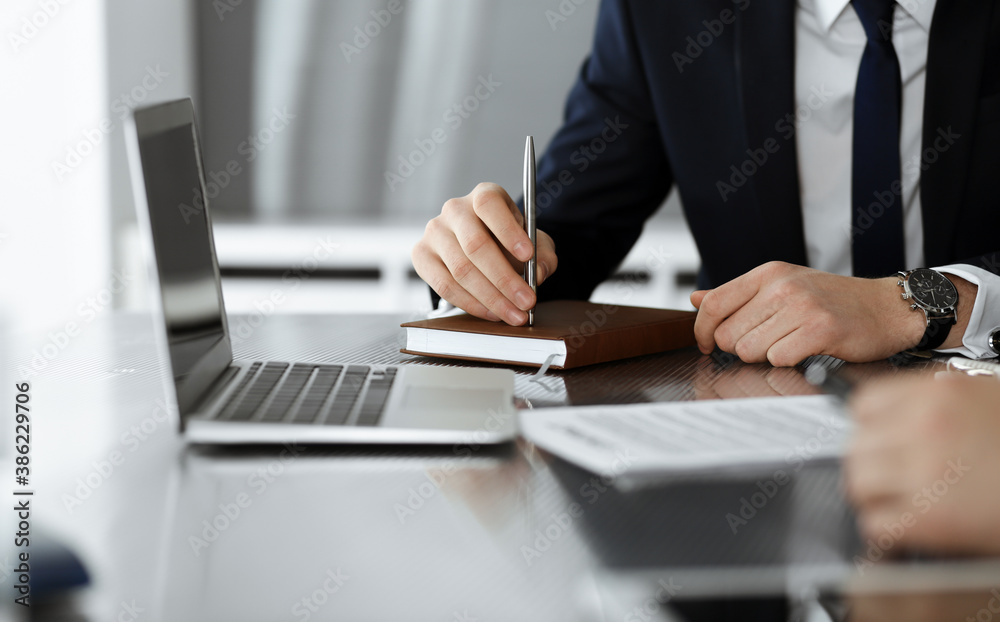 Unknown businessmen and woman sitting, using laptop computer and discussing questions at meeting in modern office, close-up Unknown businessmen and woman sitting, using laptop computer and discussing questions at meeting in modern office, close-up