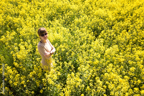 Aerial view of a young woman standing in yellow blooming rapeseed field. © bilanol