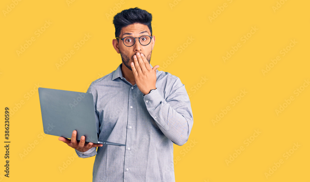 Handsome latin american young man working using computer laptop covering mouth with hand, shocked and afraid for mistake. surprised expression Handsome latin american young man working using computer laptop covering mouth with hand, shocked and afraid for mistake. surprised expression