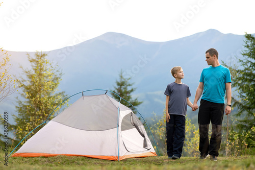 Father with his child son walking together near a tent in summer mountains. Active family recreation concept.