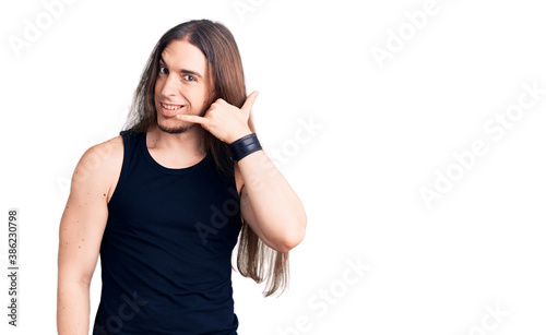 Young adult man with long hair wearing goth style with black clothes smiling doing phone gesture with hand and fingers like talking on the telephone. communicating concepts.