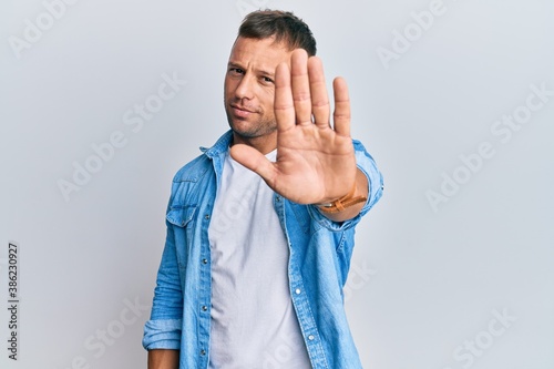 Handsome muscle man wearing casual denim jacket doing stop sing with palm of the hand. warning expression with negative and serious gesture on the face.