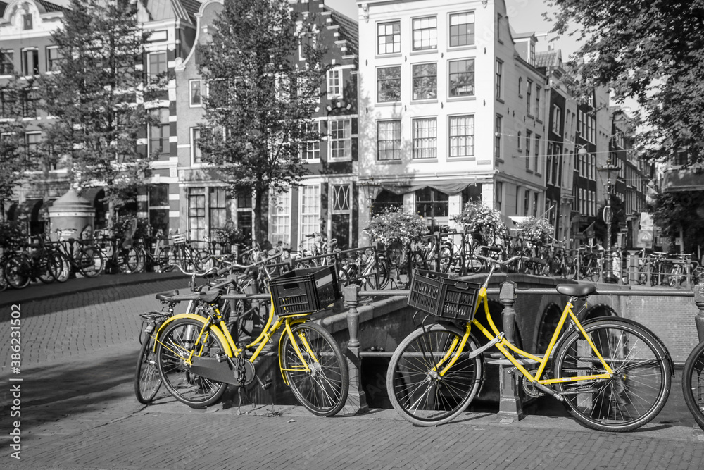 A picture of a two yellow bikes on the bridge over the channel in Amsterdam. The background is black and white.
