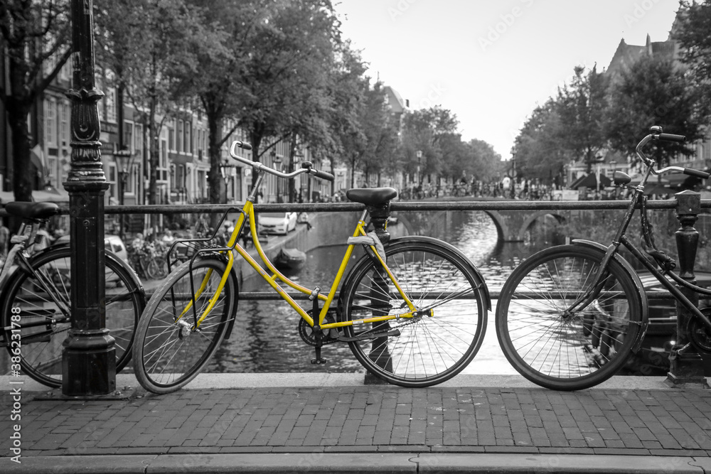 A picture of a lonely yellow bike on the bridge over the channel in Amsterdam. The background is black and white.