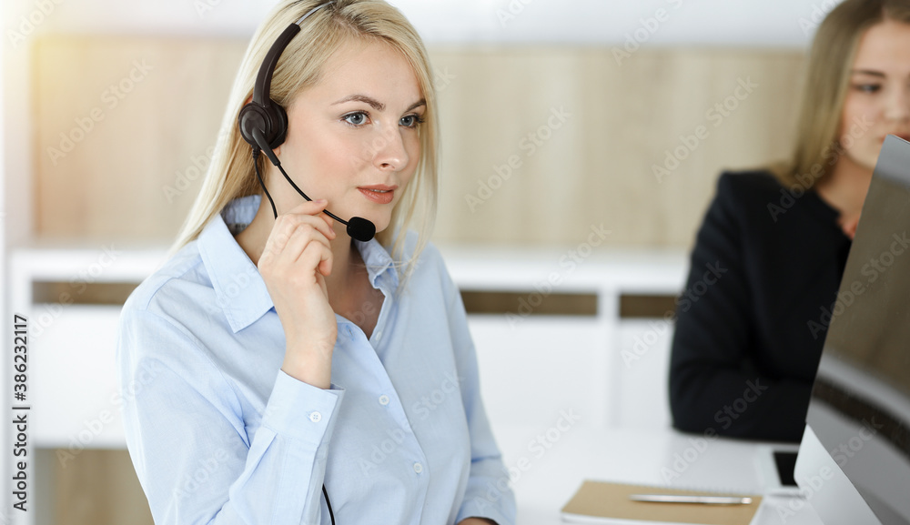Blonde business woman sitting and communicated by headset in sunny call center office Blonde business woman sitting and communicated by headset in sunny call center office