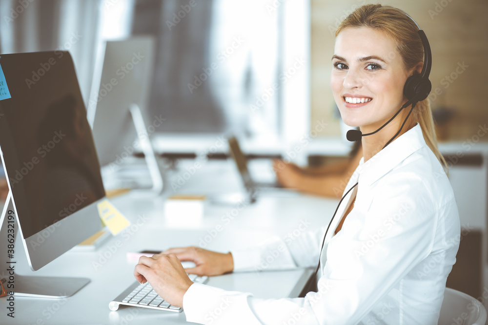 Blonde business woman using headset for communication and consulting people at customer service office. Call center. Group of operators at work Blonde business woman using headset for communication and consulting people at customer service office. Call center. Group of operators at work