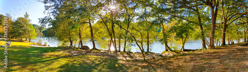 a breathtaking panoramic shot of the lush green trees on the banks of the lake with the sun peek through the trees at Morgan Falls Overlook Park in Sandy Springs
