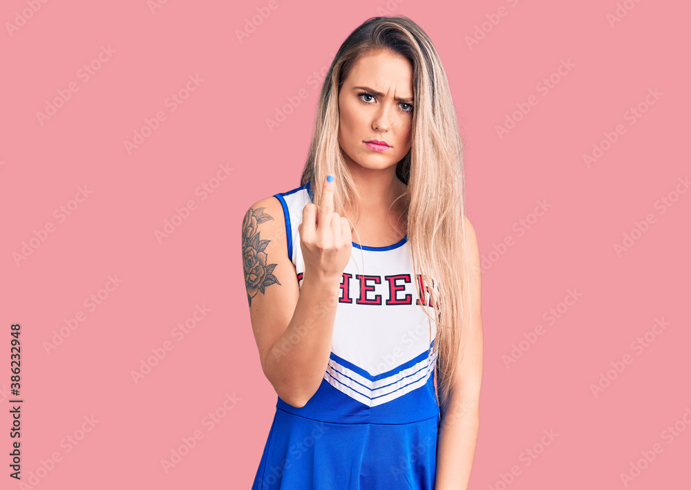 Young beautiful blonde woman wearing cheerleader uniform showing middle finger, impolite and rude fuck off expression Young beautiful blonde woman wearing cheerleader uniform showing middle finger, impolite and rude fuck off expression
