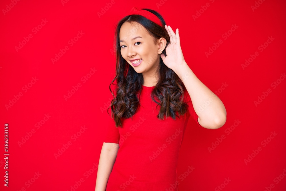 Young beautiful chinese girl wearing casual clothes smiling with hand over ear listening and hearing to rumor or gossip. deafness concept. Young beautiful chinese girl wearing casual clothes smiling with hand over ear listening and hearing to rumor or gossip. deafness concept.