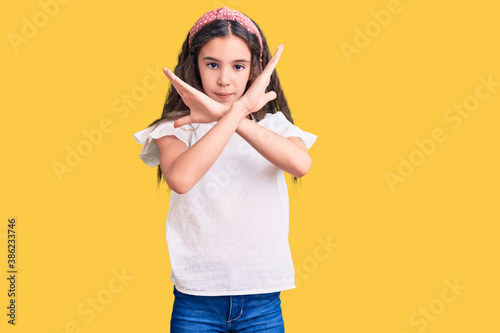 Cute hispanic child girl wearing casual white tshirt rejection expression crossing arms doing negative sign, angry face