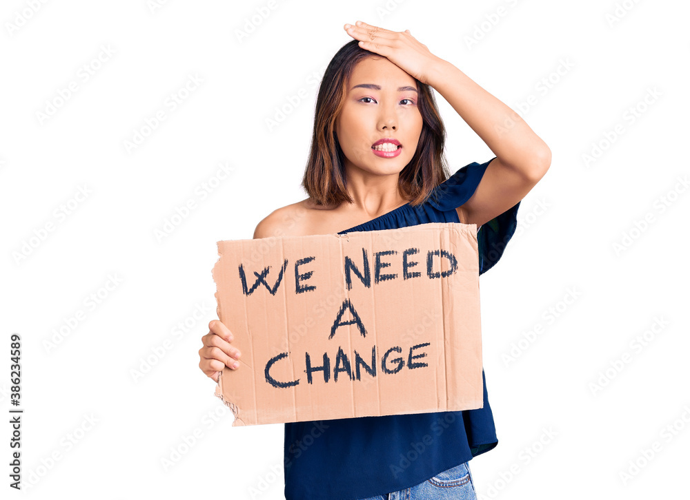 Young beautiful chinese girl holding we need a change banner stressed and frustrated with hand on head, surprised and angry face Young beautiful chinese girl holding we need a change banner stressed and frustrated with hand on head, surprised and angry face