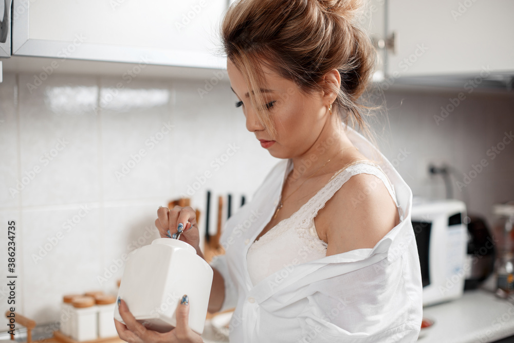 young beautiful Asian girl in beige lace shorts,white shirt adds sugar to coffee. selective focus. small focus area young beautiful Asian girl in beige lace shorts,white shirt adds sugar to coffee. selective focus. small focus area