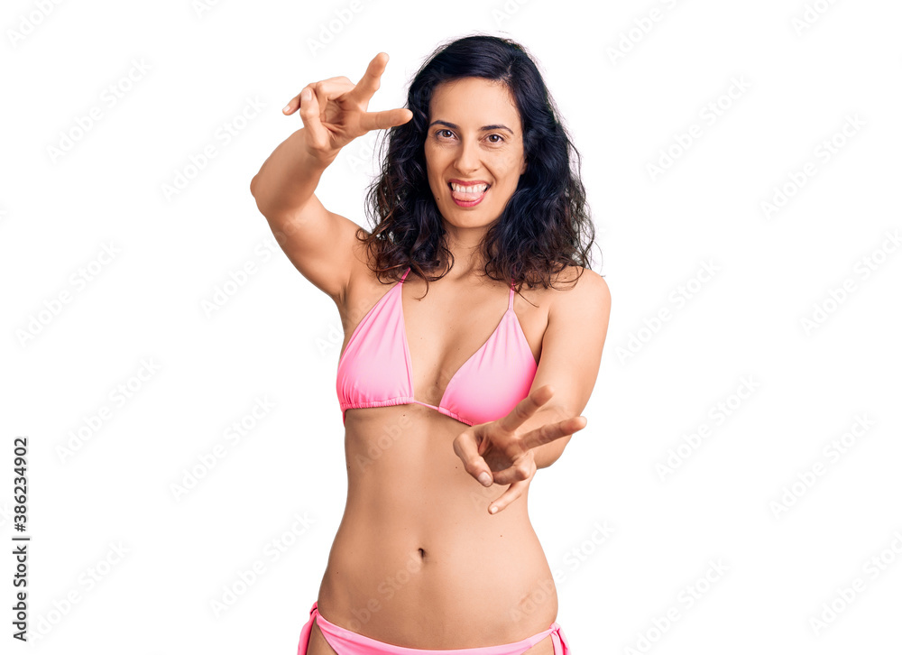 Young beautiful hispanic woman wearing bikini smiling with tongue out showing fingers of both hands doing victory sign. number two. Young beautiful hispanic woman wearing bikini smiling with tongue out showing fingers of both hands doing victory sign. number two.