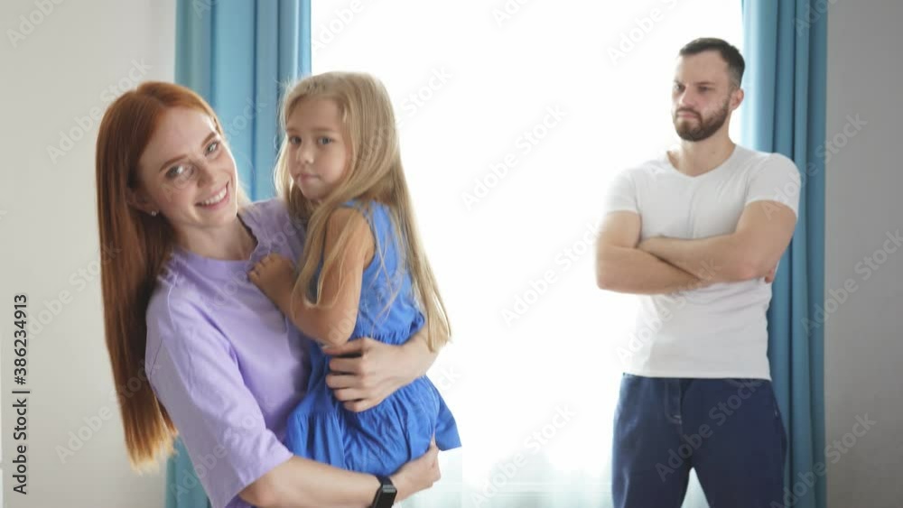 Happy caucasian women hold daughter in hands at home, they smile, offended husband does not receive attention from them. Happy caucasian women hold daughter in hands at home, they smile, offended husband does not receive attention from them.