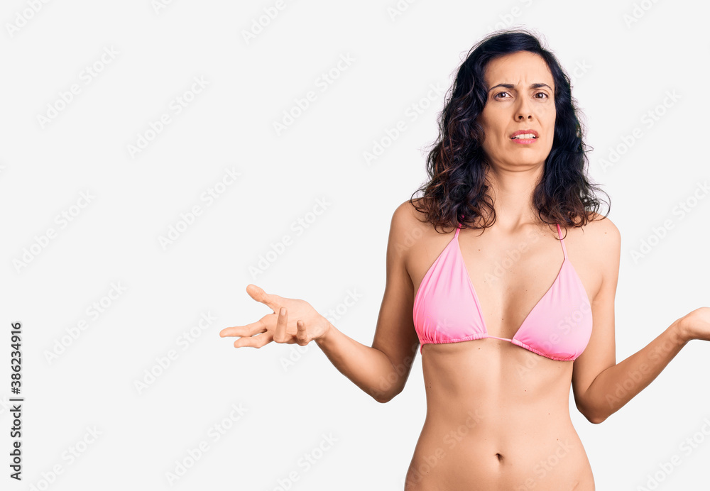 Young beautiful hispanic woman wearing bikini clueless and confused with open arms, no idea concept. Young beautiful hispanic woman wearing bikini clueless and confused with open arms, no idea concept.