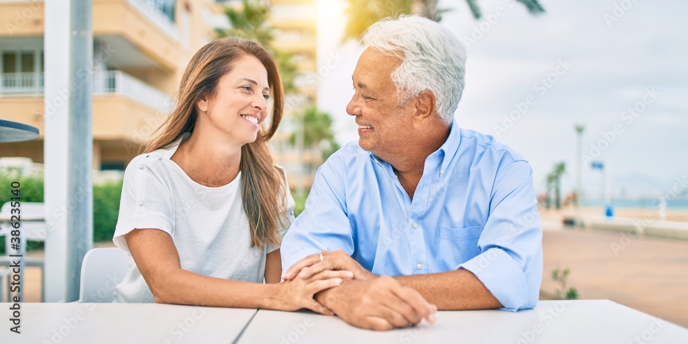 Obraz premium Middle age couple in love sitting at the terrace of coffee shop happy and cheerful together