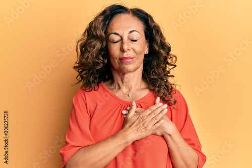 Obraz na plátně Middle age hispanic woman wearing casual clothes smiling with hands on chest with closed eyes and grateful gesture on face