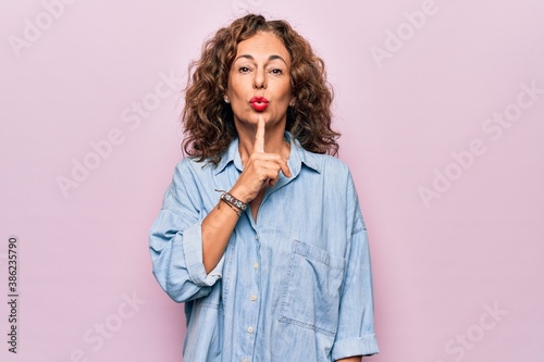Middle age beautiful woman wearing casual denim shirt standing over pink background Thinking concentrated about doubt with finger on chin and looking up wondering