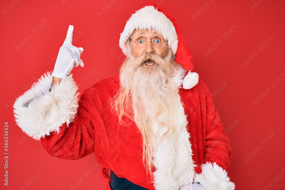 Old senior man with grey hair and long beard wearing traditional santa claus costume pointing finger up with successful idea. exited and happy. number one.